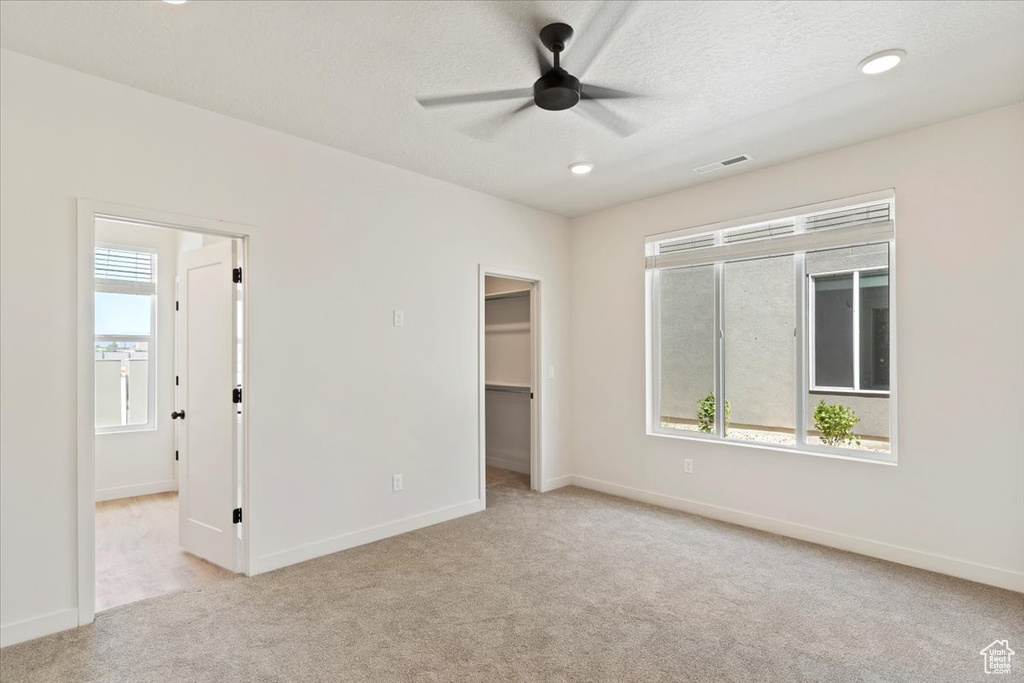 Unfurnished bedroom featuring light carpet, a walk in closet, recessed lighting, ceiling fan, and a closet