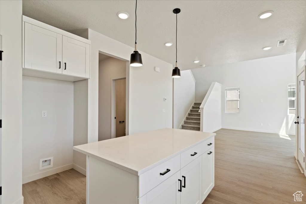 Kitchen featuring light wood-type flooring, a kitchen island, recessed lighting, white cabinets, and decorative light fixtures