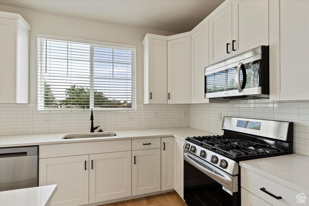 Kitchen featuring stainless steel appliances, white cabinetry, tasteful backsplash, and light countertops