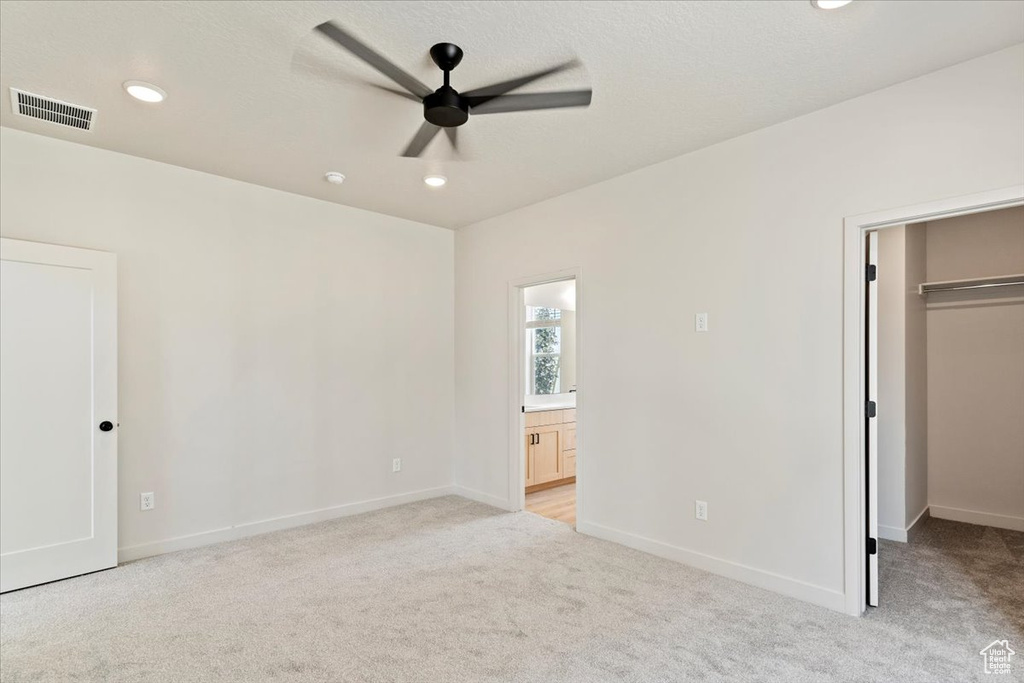 Unfurnished bedroom featuring a walk in closet, light carpet, recessed lighting, ensuite bathroom, and a closet