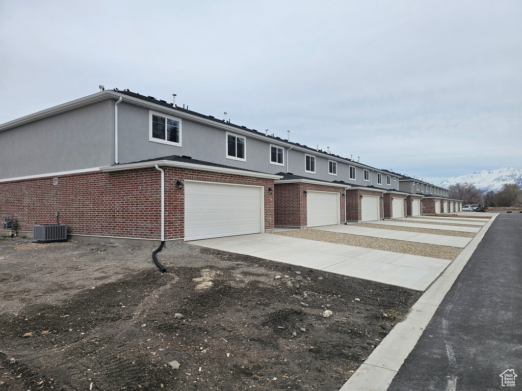 Townhome / multi-family property featuring a garage, central AC, brick siding, and driveway