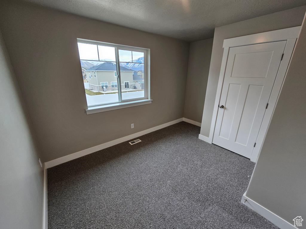 Unfurnished bedroom featuring dark colored carpet, visible vents, a textured ceiling, and baseboards