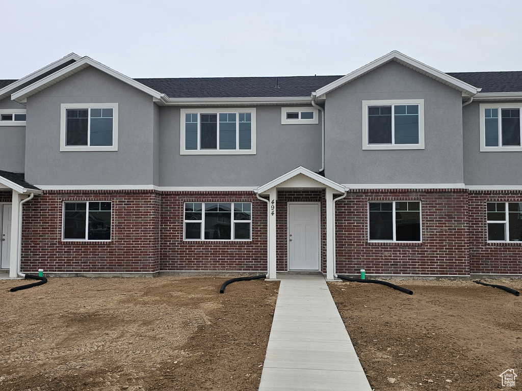 Townhome / multi-family property with brick siding, a shingled roof, and stucco siding