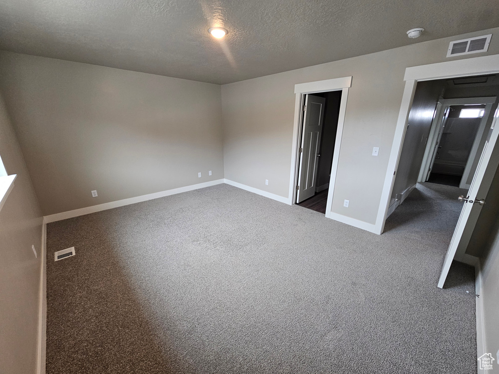 Unfurnished bedroom featuring a textured ceiling, dark colored carpet, visible vents, and baseboards