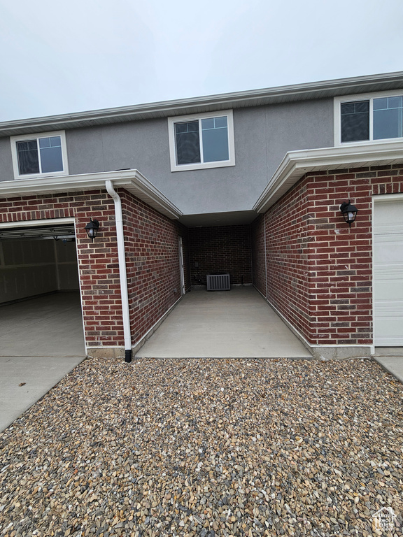 Exterior space featuring brick siding, stucco siding, a garage, cooling unit, and driveway