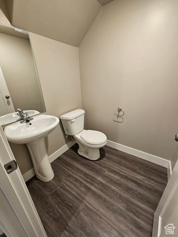 Bathroom with lofted ceiling, wood finished floors, toilet, and baseboards