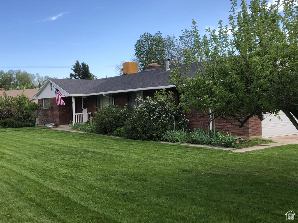 View of front facade with brick siding, a front yard, a shingled roof, and a chimney