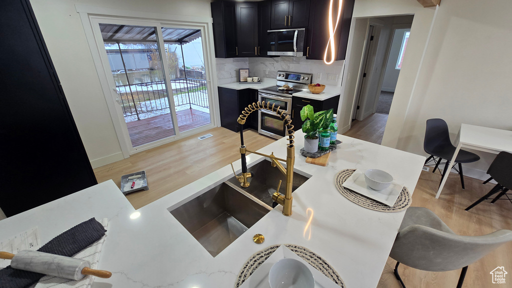 Kitchen with baseboards, decorative backsplash, appliances with stainless steel finishes, dark cabinetry, and light wood-type flooring