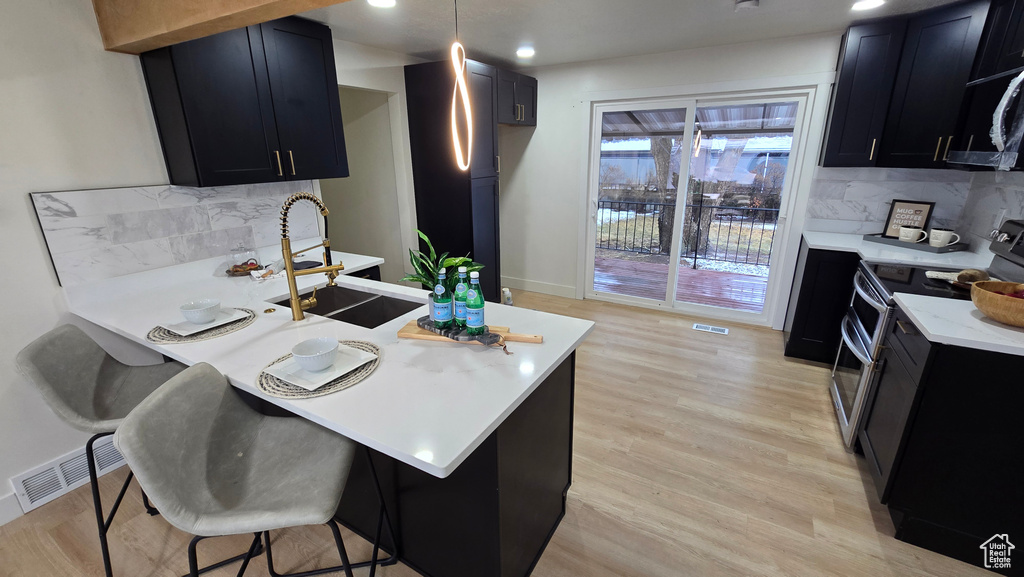 Kitchen with range with two ovens, visible vents, a kitchen breakfast bar, dark cabinetry, and decorative light fixtures