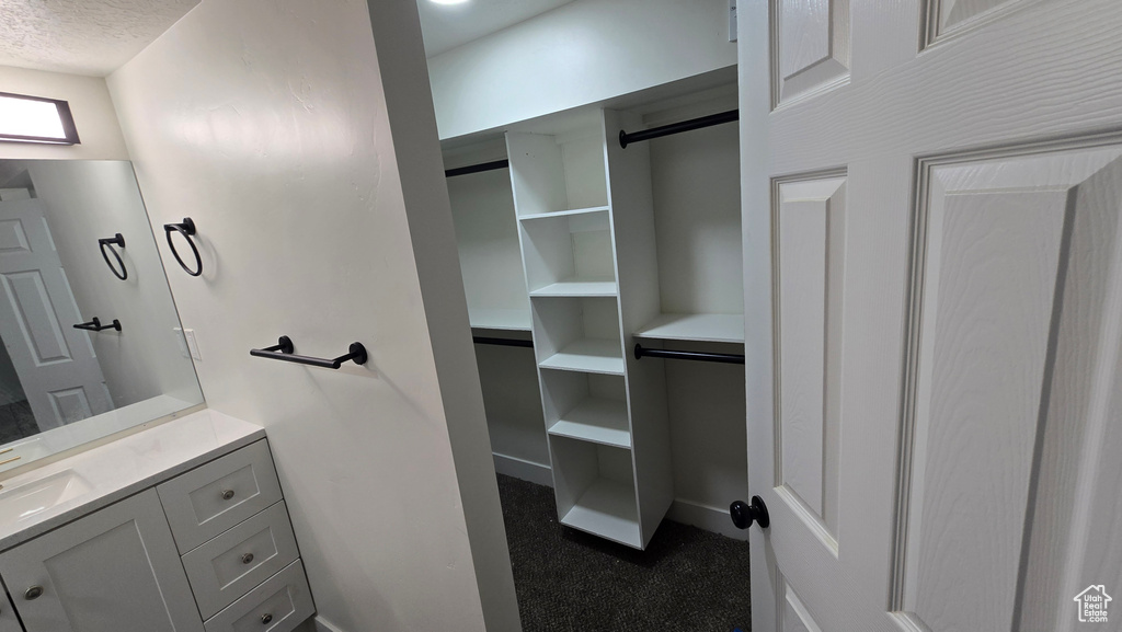 Bathroom featuring a textured ceiling, a spacious closet, vanity, and baseboards