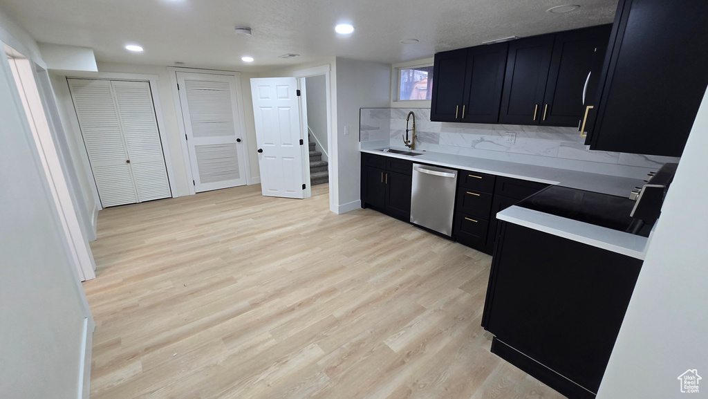 Kitchen with dishwasher, light countertops, dark cabinetry, light wood-style floors, and a sink