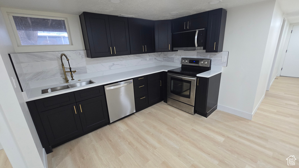 Kitchen with a sink, stainless steel appliances, dark cabinetry, and light countertops