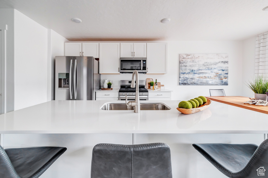 Kitchen featuring light countertops, appliances with stainless steel finishes, a breakfast bar area, and white cabinetry