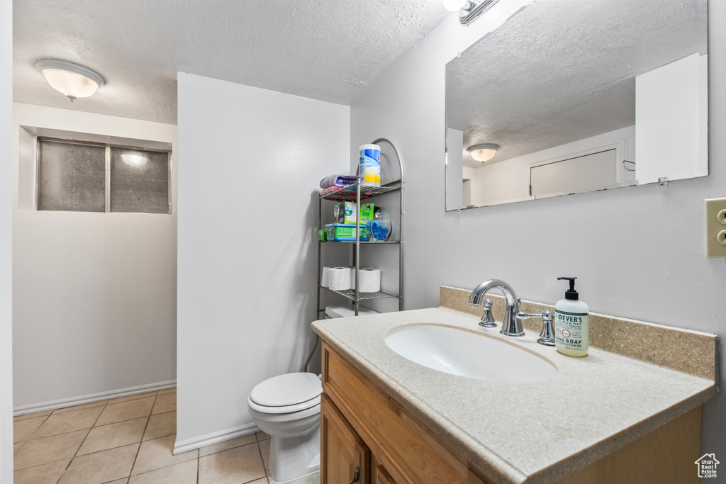 Half bathroom featuring toilet, tile patterned flooring, a textured ceiling, vanity, and baseboards