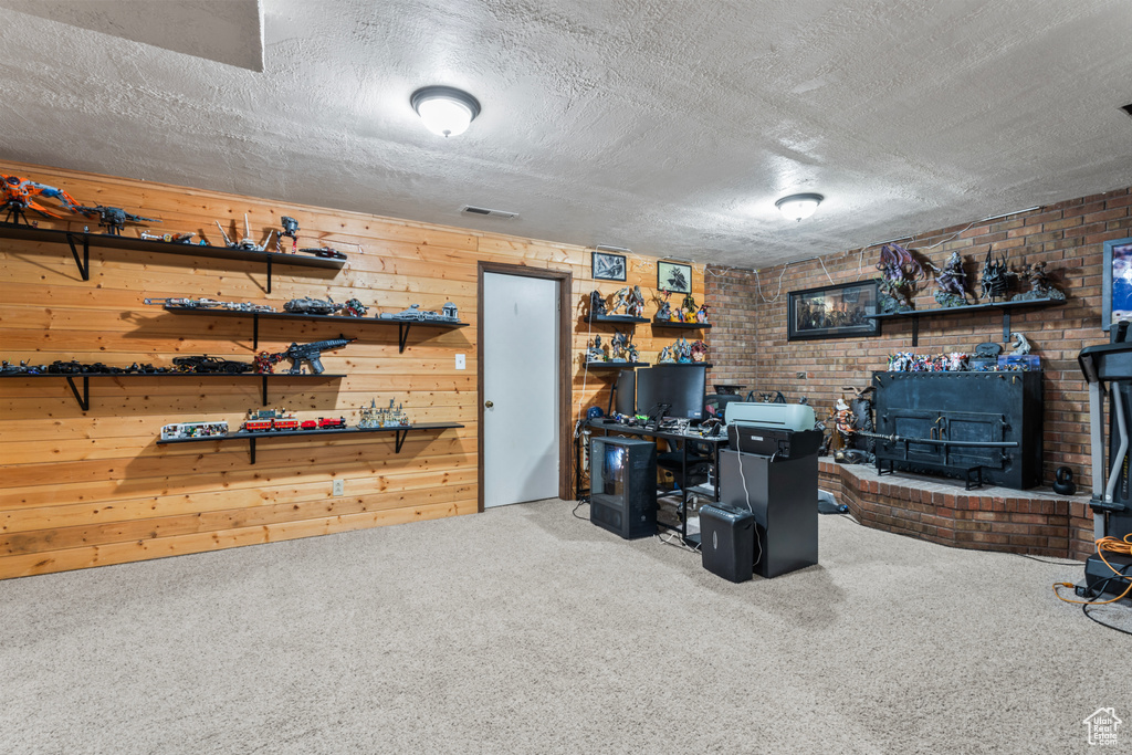 Carpeted office with a wood stove, a textured ceiling, brick wall, and wood walls