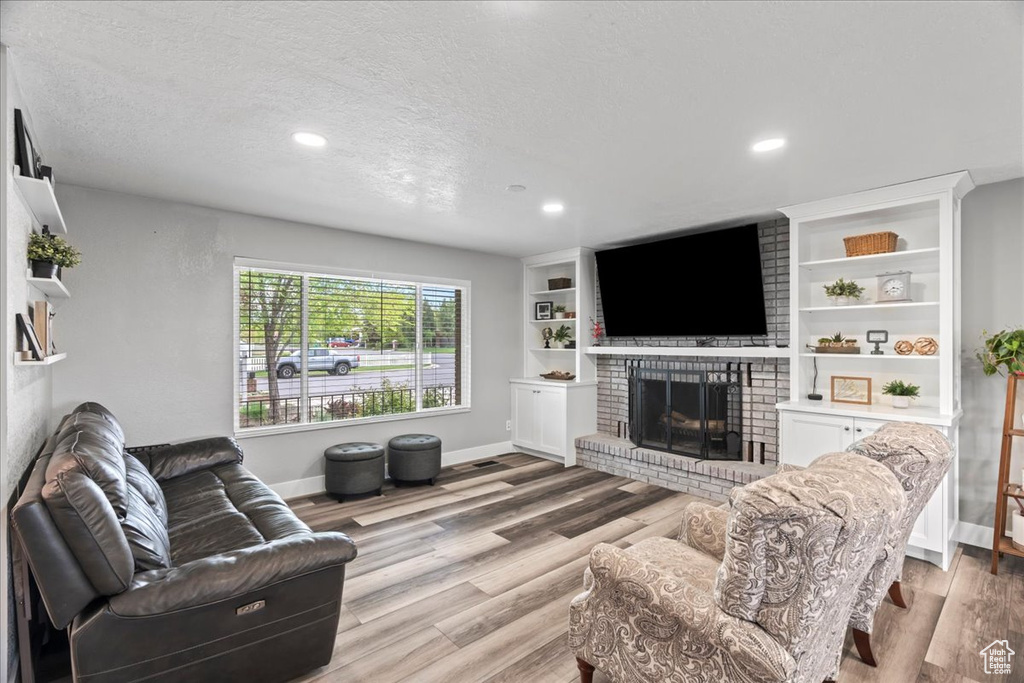 Living room featuring a brick fireplace, light wood-style flooring, baseboards, recessed lighting, and a textured ceiling