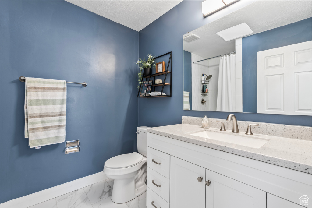 Full bathroom with toilet, baseboards, marble look tiles, vanity, and curtained shower