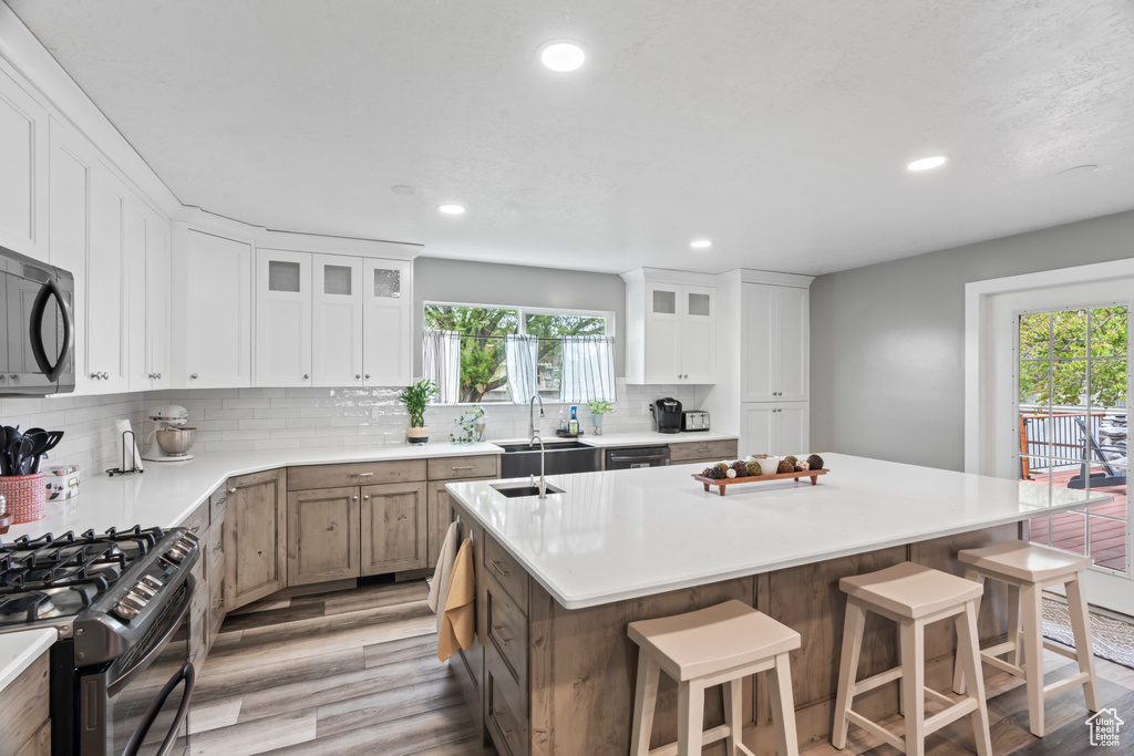 Kitchen with black appliances, light wood-style flooring, an island with sink, a breakfast bar area, and recessed lighting