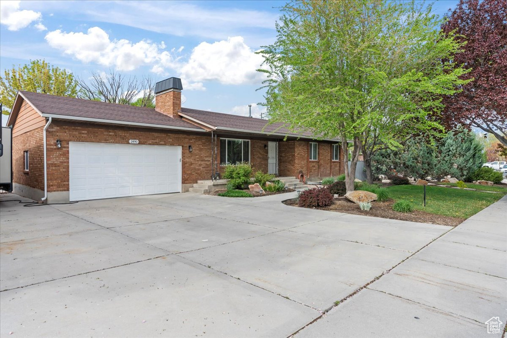 Ranch-style home featuring brick siding, a garage, driveway, and a chimney