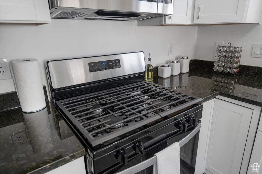 Kitchen with gas range, wall chimney exhaust hood, white cabinetry, and dark stone counters