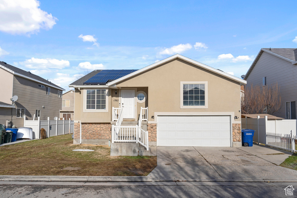 View of front facade featuring stone siding, fence, roof mounted solar panels, and stucco siding