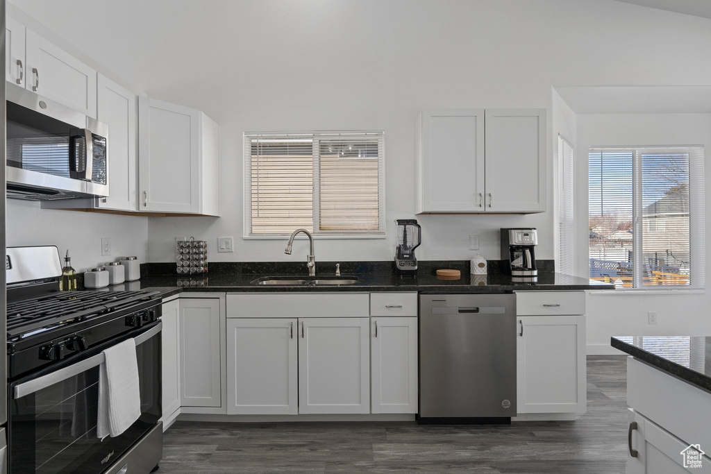 Kitchen with stainless steel appliances, a sink, white cabinetry, dark wood-style floors, and dark stone countertops