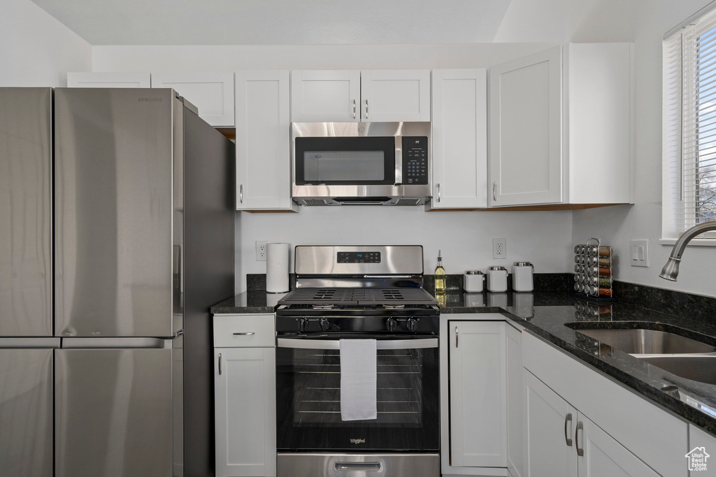 Kitchen featuring a healthy amount of sunlight, white cabinets, stainless steel appliances, and dark stone counters