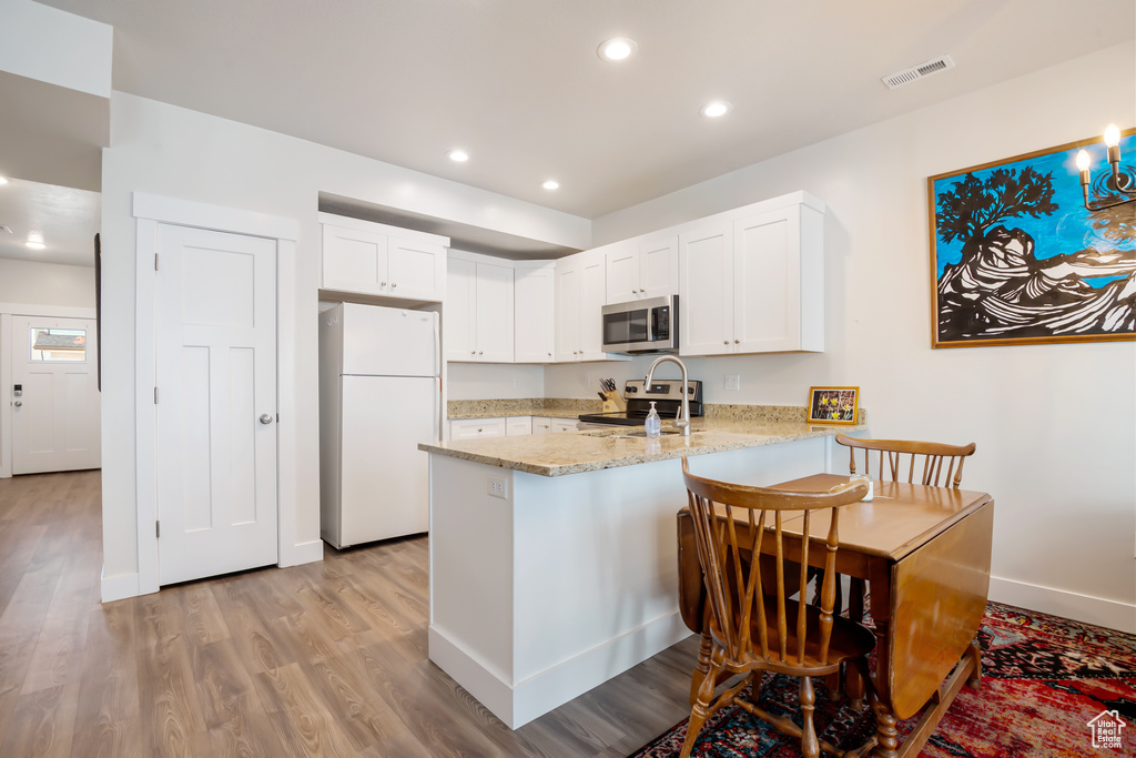 Kitchen featuring stainless steel appliances, visible vents, white cabinets, light stone countertops, and a peninsula