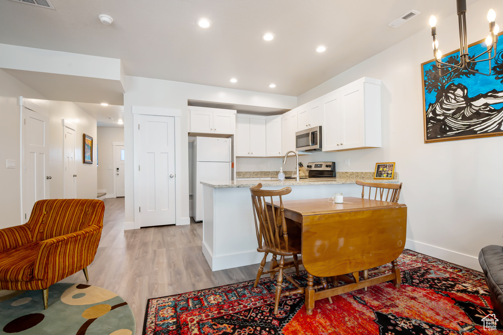 Kitchen featuring visible vents, appliances with stainless steel finishes, white cabinets, light stone countertops, and a peninsula