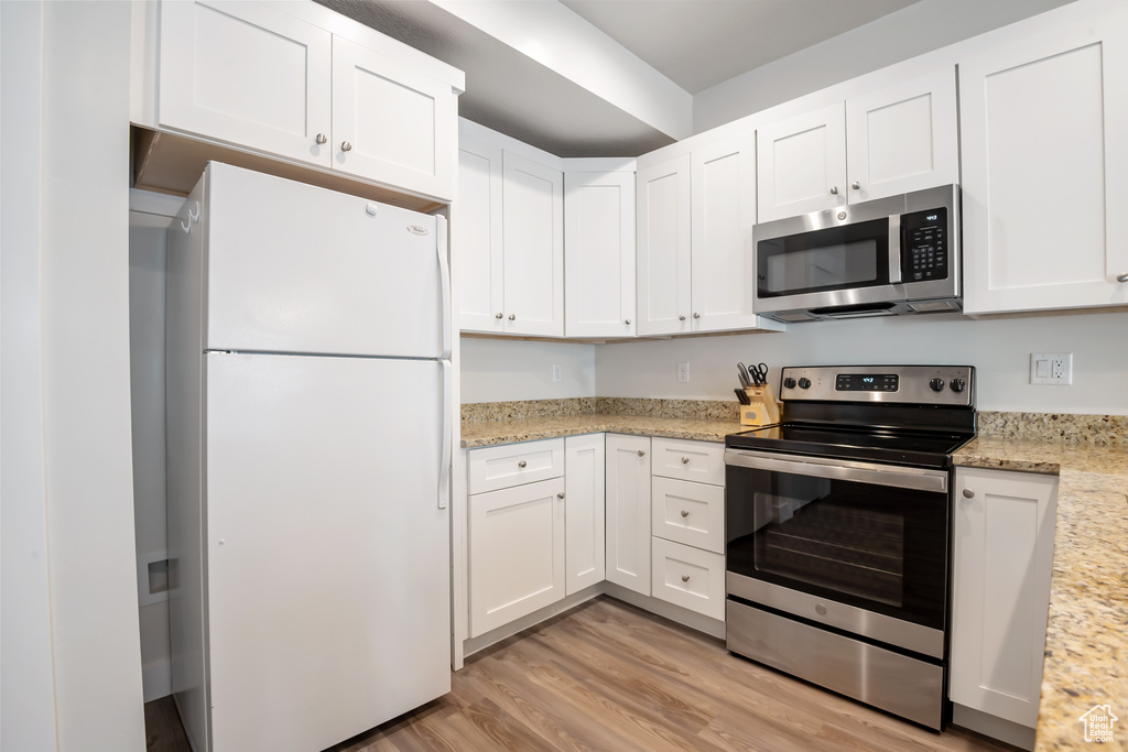 Kitchen with appliances with stainless steel finishes, light wood-type flooring, light stone countertops, and white cabinets