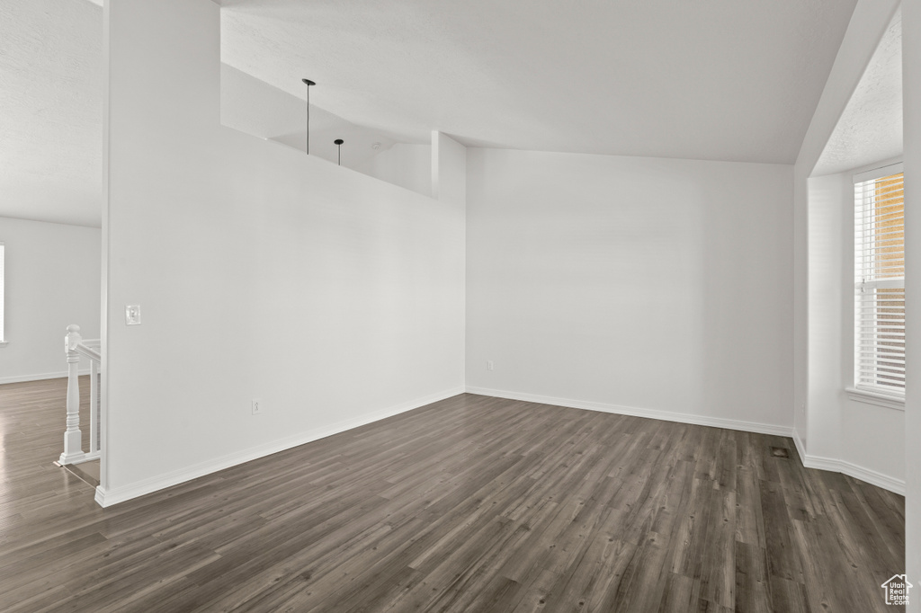 Empty room with lofted ceiling, dark wood-type flooring, and baseboards