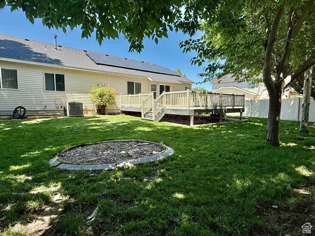 Back of property with a deck, roof mounted solar panels, and cooling unit