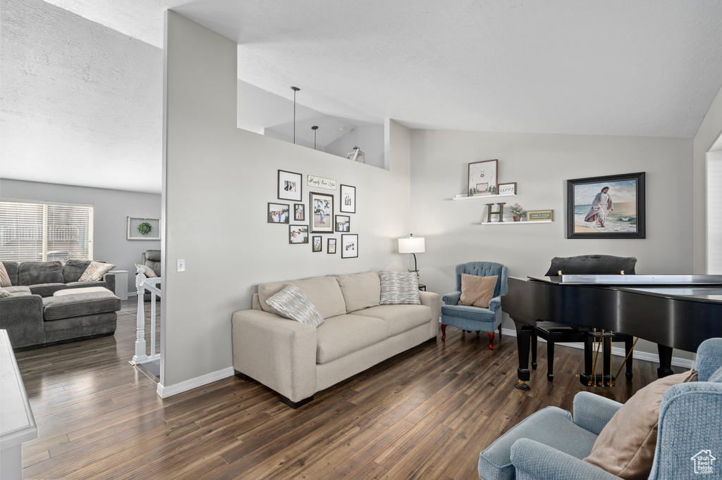 Living room with vaulted ceiling, a textured ceiling, baseboards, and wood finished floors