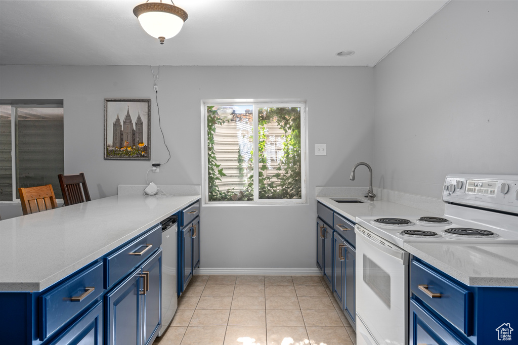 Kitchen featuring light tile patterned floors, blue cabinets, a peninsula, white electric range, and a sink