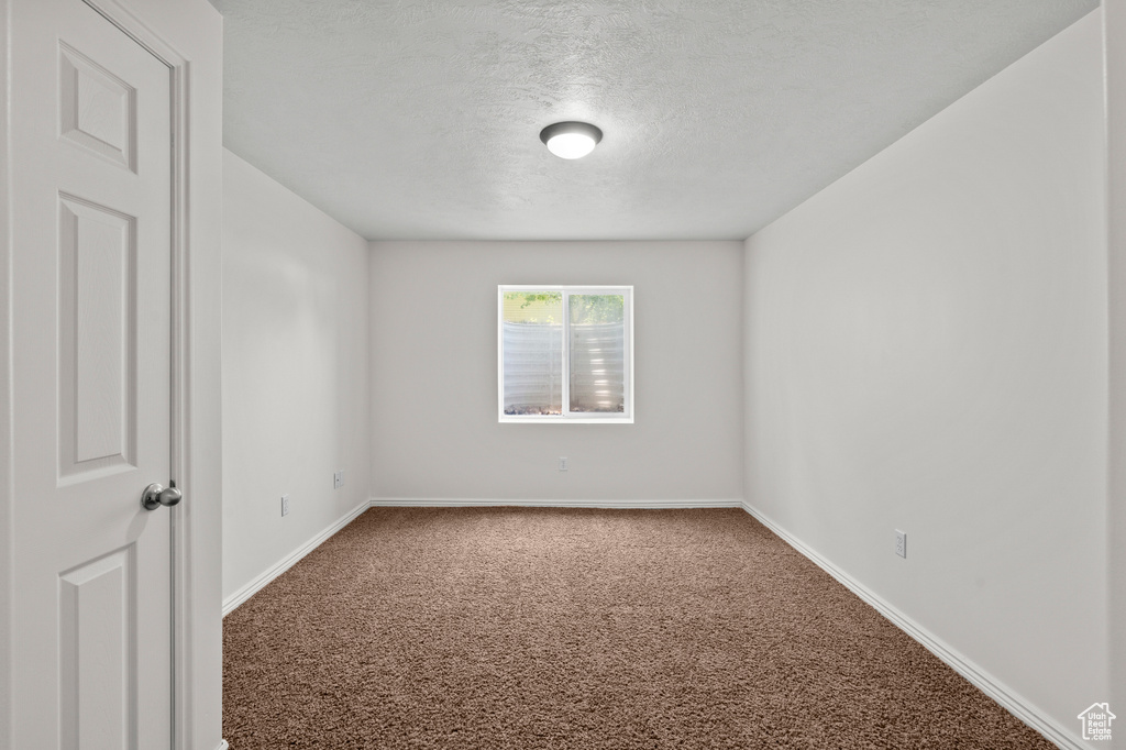 Carpeted empty room featuring a textured ceiling and baseboards