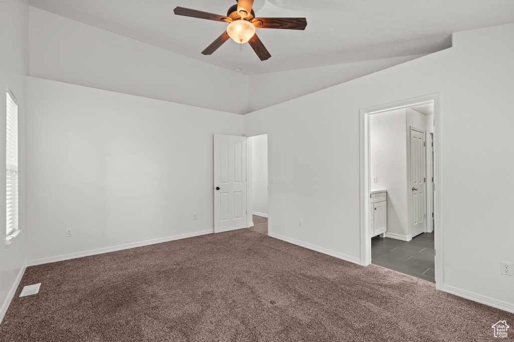 Unfurnished bedroom featuring dark carpet, vaulted ceiling, baseboards, ensuite bath, and ceiling fan
