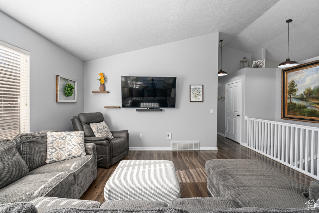Living area with lofted ceiling, visible vents, baseboards, and wood finished floors