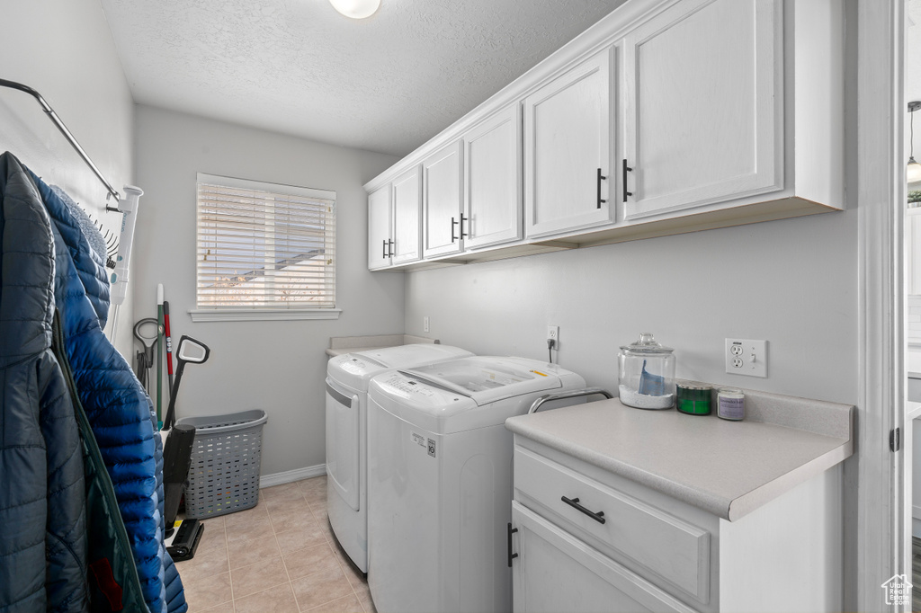 Laundry room with cabinet space, light tile patterned floors, baseboards, washer and clothes dryer, and a textured ceiling