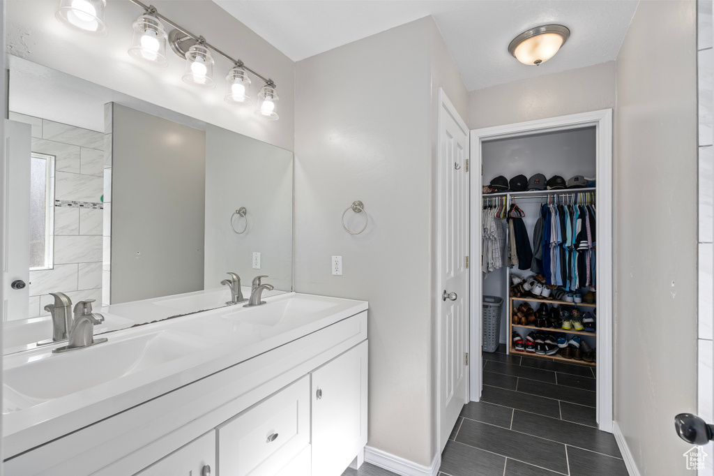 Full bathroom with double vanity, tile patterned flooring, a walk in closet, and a sink