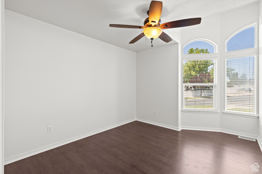 Spare room featuring dark wood-style flooring, a ceiling fan, and baseboards