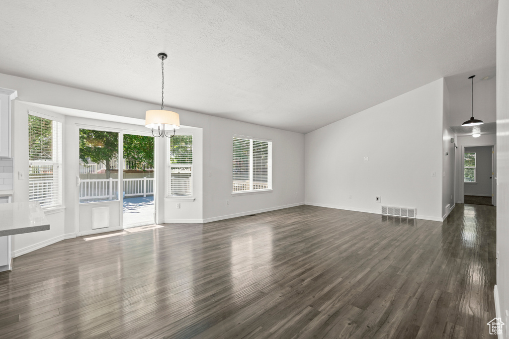Unfurnished living room with dark wood finished floors, a textured ceiling, a chandelier, and baseboards