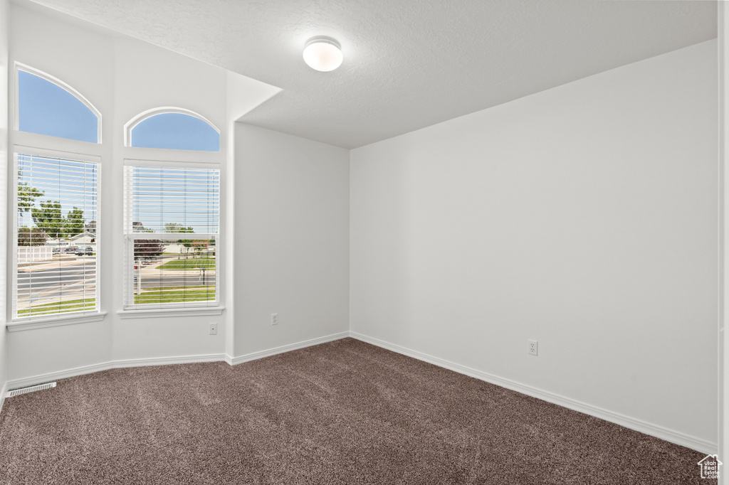 Empty room featuring dark carpet, baseboards, and a textured ceiling