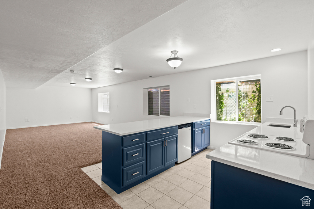 Kitchen with blue cabinetry, a peninsula, light countertops, a sink, and healthy amount of natural light