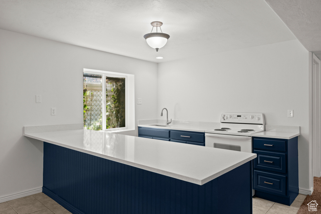 Kitchen with blue cabinetry, electric stove, a peninsula, a sink, and light tile patterned floors