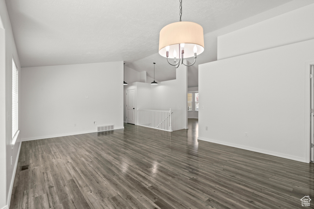 Unfurnished living room featuring dark wood-style flooring, baseboards, a chandelier, and high vaulted ceiling