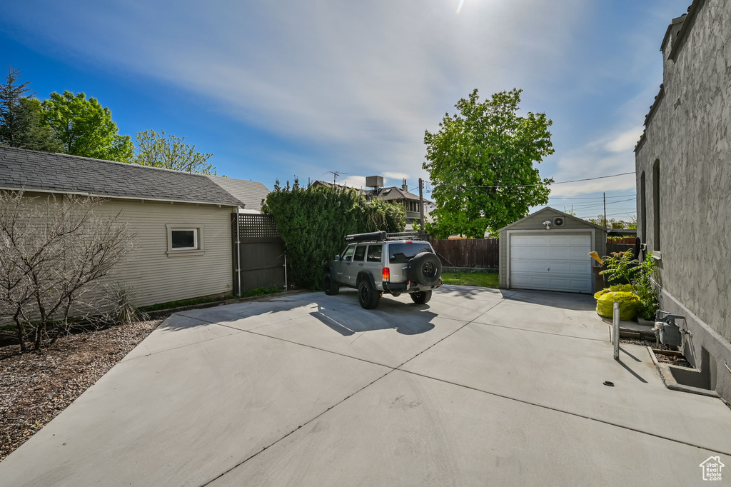 View of patio / terrace with a garage, fence, concrete driveway, and an outdoor structure