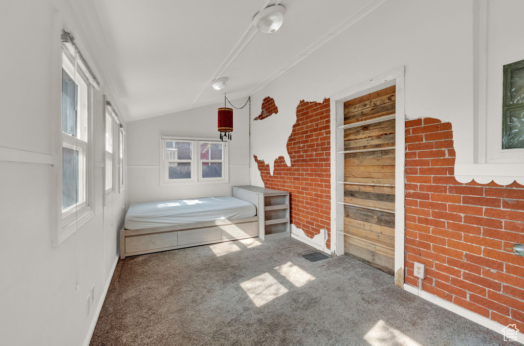 Unfurnished bedroom with carpet, vaulted ceiling, and brick wall