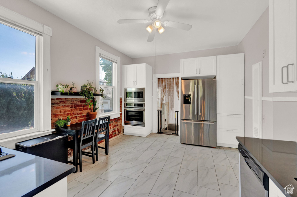 Kitchen featuring dark countertops, appliances with stainless steel finishes, white cabinets, and a ceiling fan