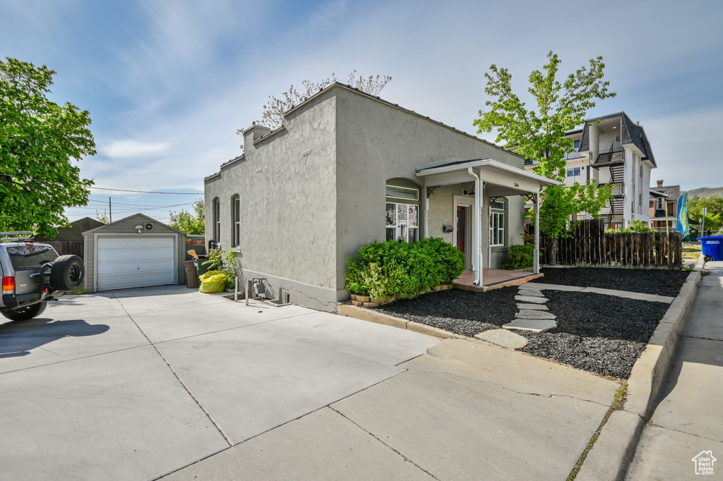 View of property exterior featuring driveway, a detached garage, an outbuilding, fence, and stucco siding