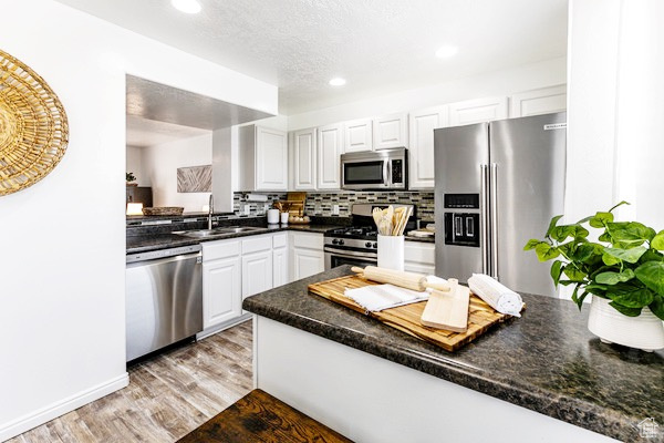 Kitchen with dark countertops, appliances with stainless steel finishes, a sink, light wood-style floors, and backsplash